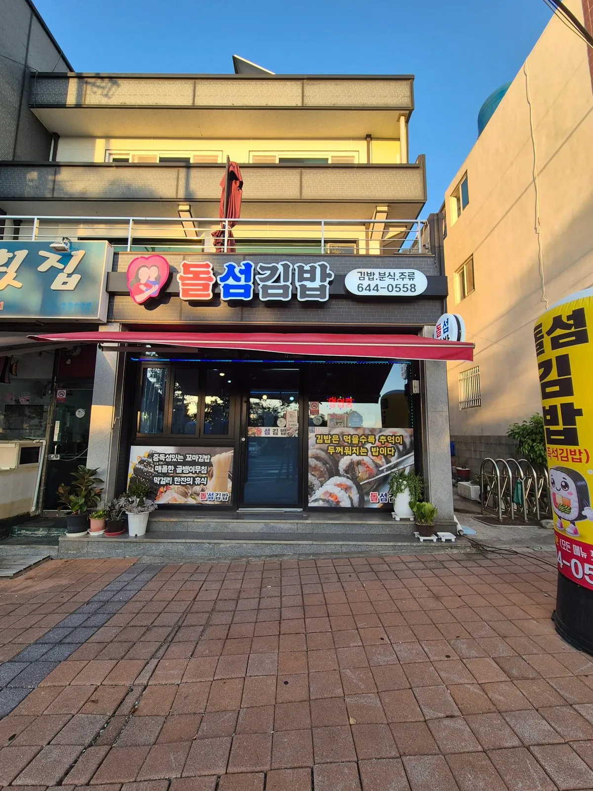 해 질 녘 돌섬김밥 외관 — 빨간 어닝과 김밥·분식·주류 간판