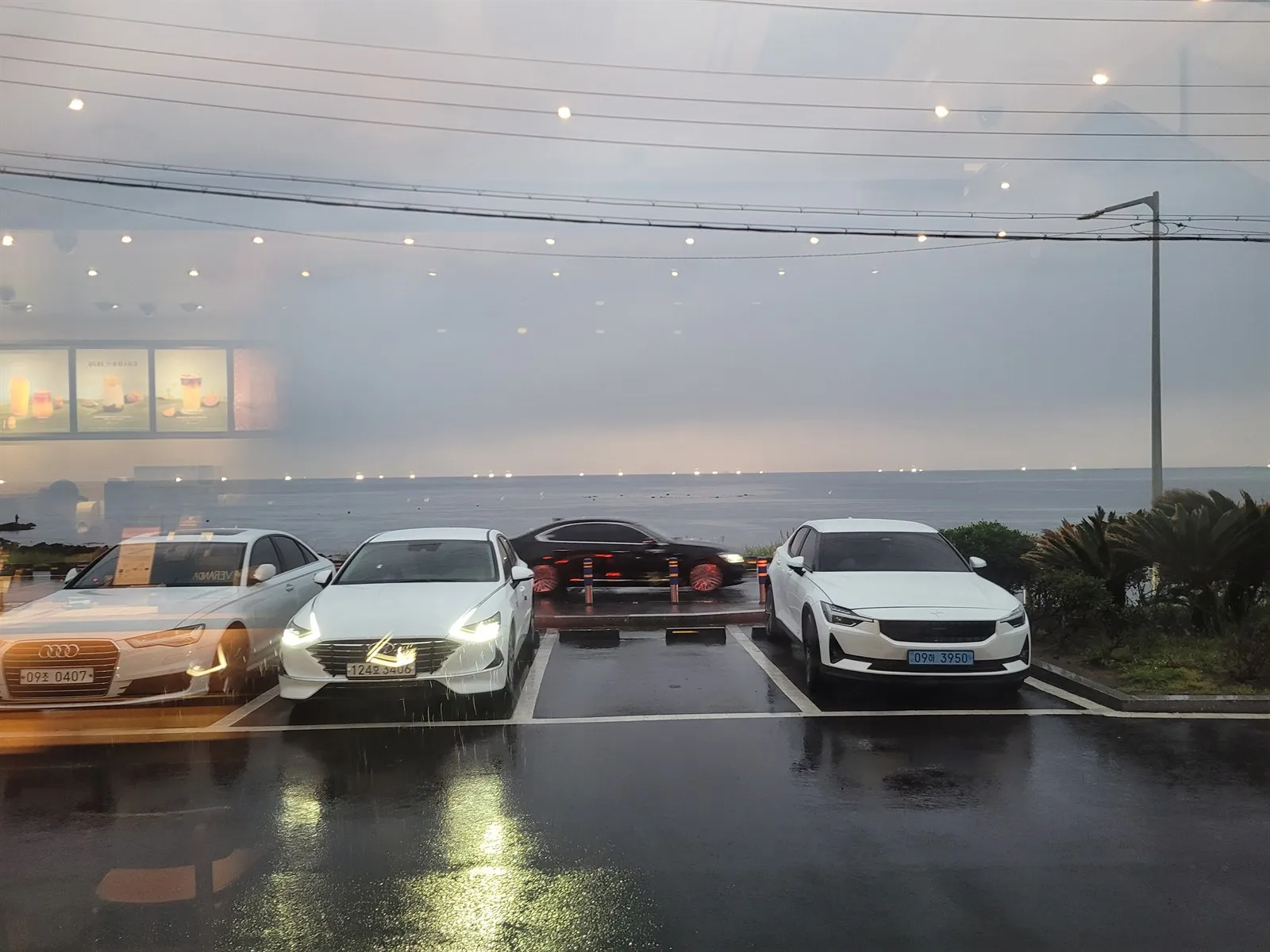 2층 창가에서 본 주차장 너머 바다, 비 오는 저녁